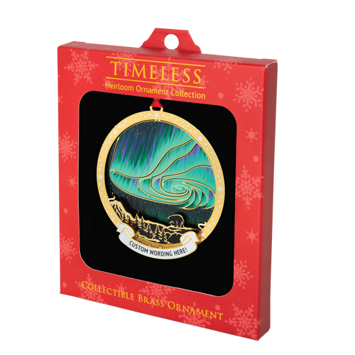 Teal and purple northern lights ornament with bear and forest silhouette in front. Has a circular brass frame with stars and a white banner at the bottom that reads “CUSTOM WORDING HERE!” in black. It is inside a red “Timeless” box with window.