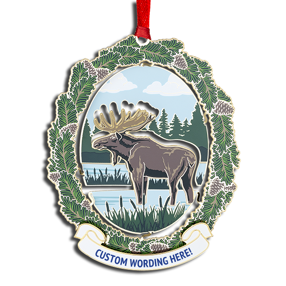 Ornament of a brown moose standing in a river with trees in the background. It has a green pine branch frame and a white banner at the bottom that reads “CUSTOM WORDING HERE!” in blue.