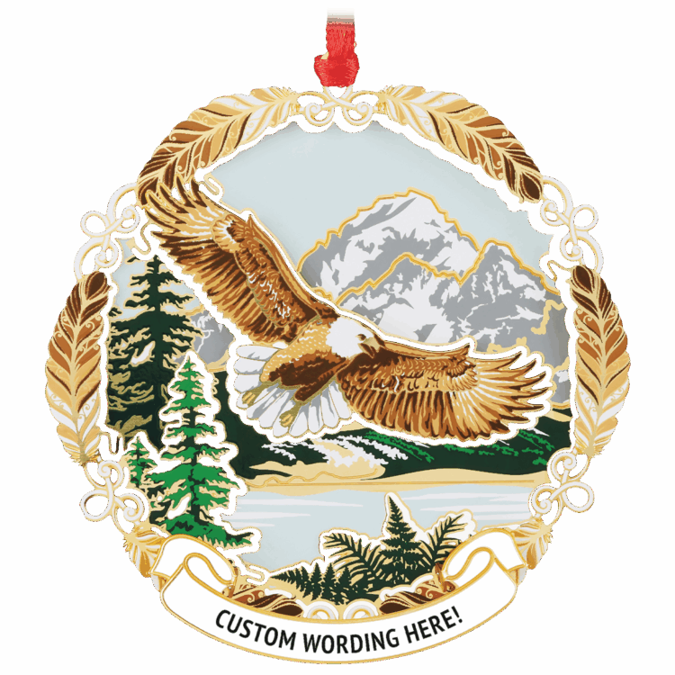 Ornament of a brown eagle flying over a light blue river with a green and white mountain scene in the back. It has a brown feather frame and a white banner at the bottom that reads “CUSTOM WORDING HERE!” in black.