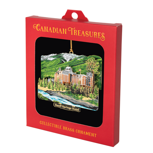 Multi-layered ornament with white and green mountains in the back, a brown castle-type building in the centre and a blue river in the front. A black plaque below reads “Banff Springs Hotel” in brass lettering. It is inside a red “Canadian Treasures” box with window.